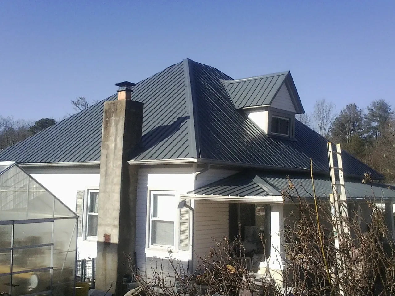 Dark blue standing seam metal roof on a white farmhouse with dormer — Slate & Tile Roof Repair by Roofing Brothers in Fort Eustis