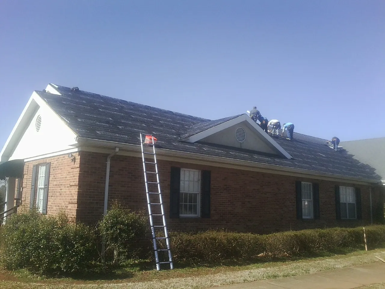 Crew tearing shingles off a brick ranch roof with a ladder set — Metal Roof Repair work by our crew in Fort Eustis