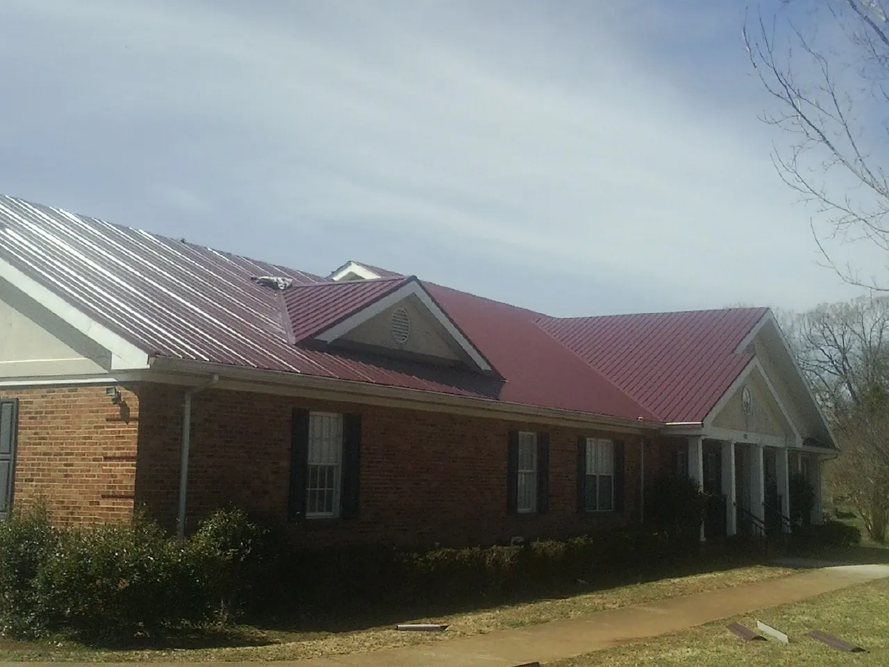 Red metal roof with gabled entries on a long brick building, from a Hail Damage Roof Repair job in Fort Eustis