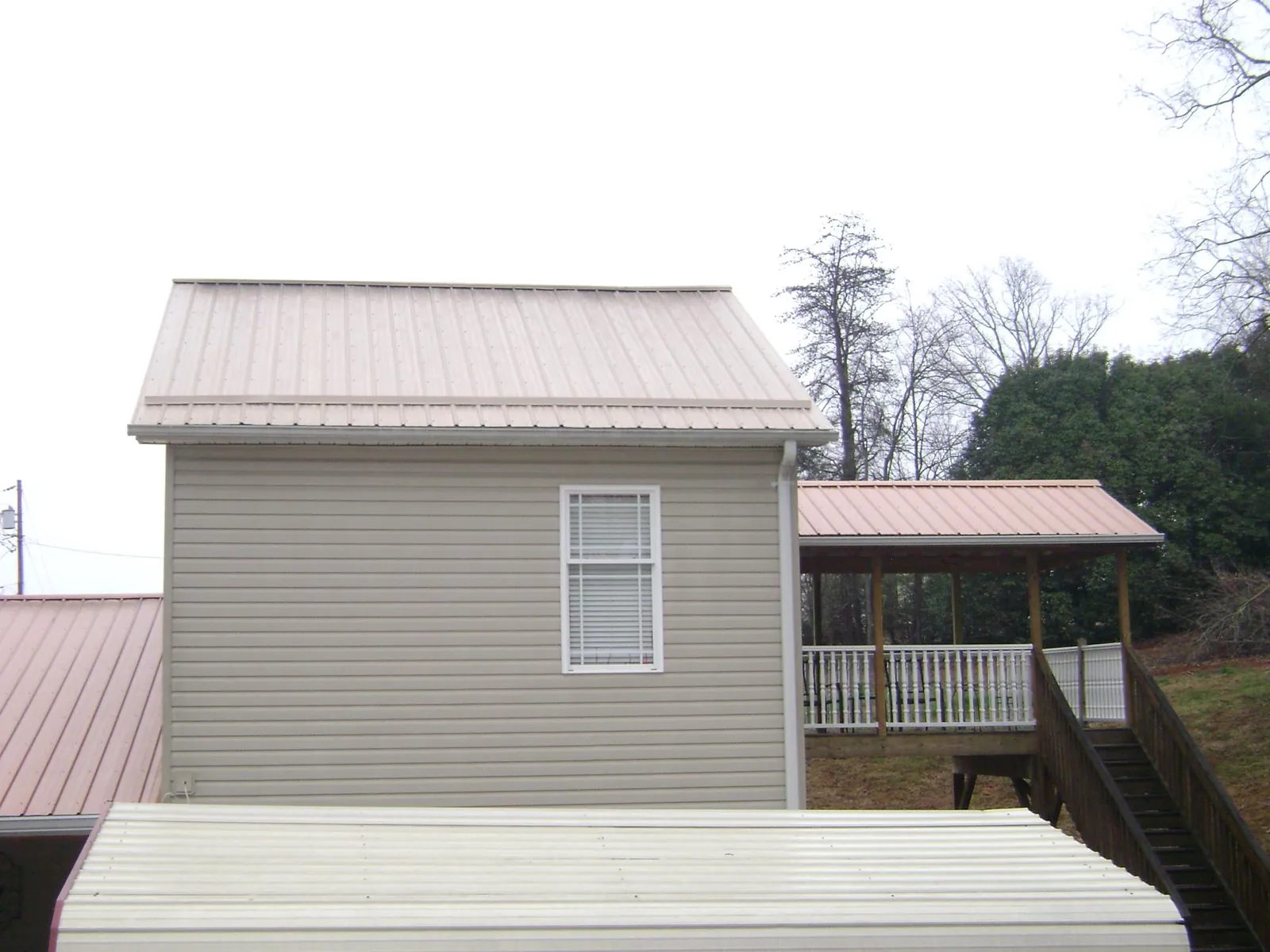 Tan metal roofs on a two story addition and attached porch, from a Roof Replacement job in Fort Eustis